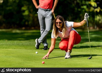 Couple playing golf, young woman reading green, getting ready to putt