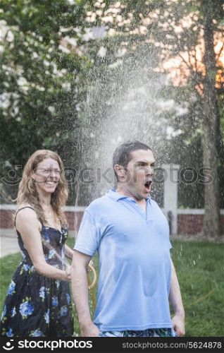 Couple playing with a garden hose and spraying each other outside in the garden, man has a shocked look