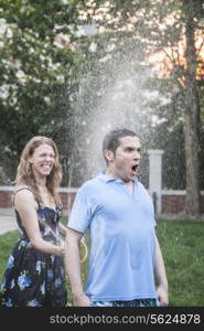 Couple playing with a garden hose and spraying each other outside in the garden, man has a shocked look