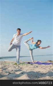 Couple practicing yoga at the beach