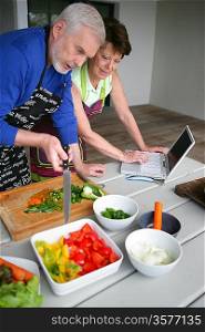 Couple preparing vegetables and looking at a laptop
