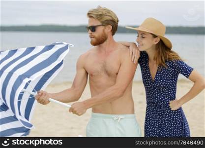 couple putting down the parasol on the beach