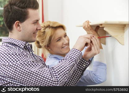 Couple Putting Up Wooden Shelf Together At Home