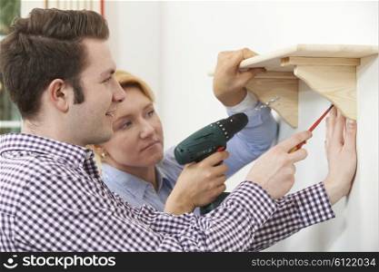 Couple Putting Up Wooden Shelf Together At Home