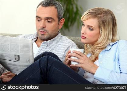 Couple reading newspaper on couch