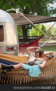 Couple reclining on hammock next to converted boutique airstream trailer