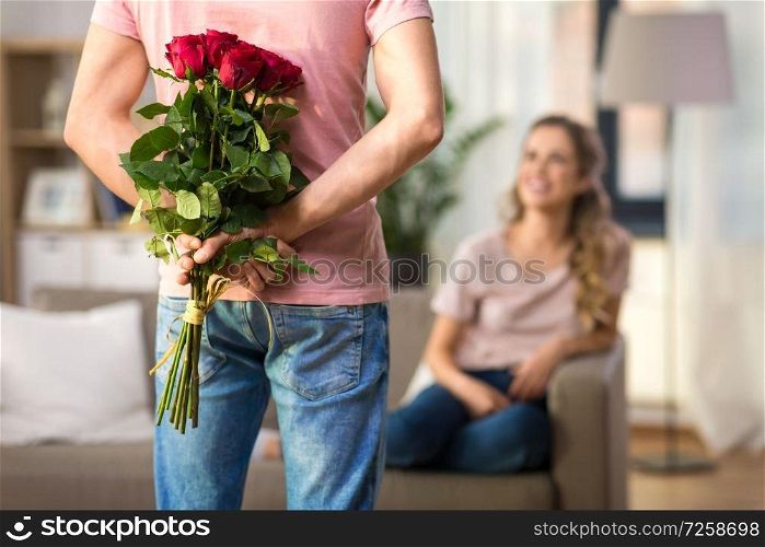 couple, relationships and people concept - happy woman looking at man hiding bunch of roses behind his back. woman and man with bunch of roses behind his back