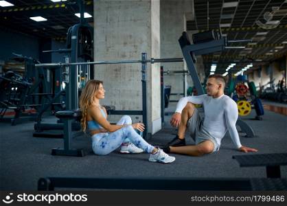 Couple relax on the floor after fitness training in gym. Athletic man and woman on workout in sport club, active healthy lifestyle. Couple relax after fitness training in gym