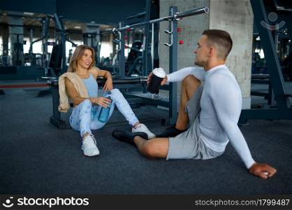 Couple relax on the floor after fitness training in gym. Athletic man and woman on workout in sport club, active healthy lifestyle, physical wellness. Couple relax after fitness training in gym