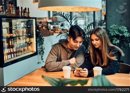 Couple relaxing in a cafe, using smartphone, having a chat, talking together, drinking coffee. Young man and woman having a break, spending time together