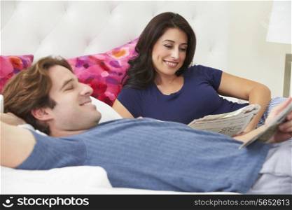 Couple Relaxing In Bed Wearing Pajamas And Reading Newspaper