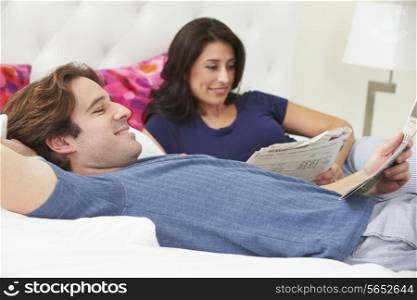 Couple Relaxing In Bed Wearing Pajamas And Reading Newspaper