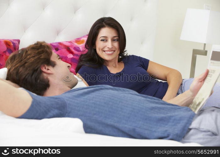 Couple Relaxing In Bed Wearing Pajamas And Reading Newspaper