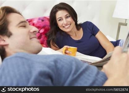 Couple Relaxing In Bed With Coffee And Newspaper