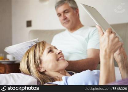 Couple Relaxing In Bed With Newspaper And Digital Tablet