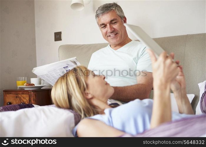 Couple Relaxing In Bed With Newspaper And Digital Tablet