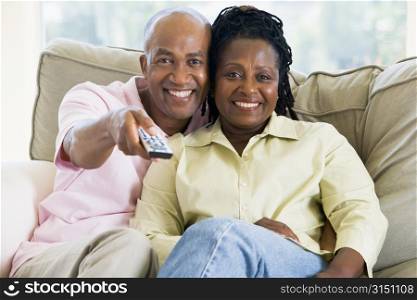 Couple relaxing in living room holding remote control and smiling