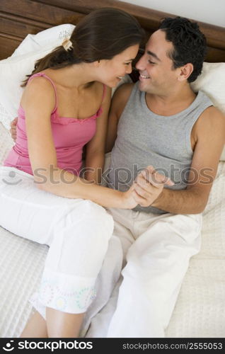 Couple relaxing on bed holding hands in bedroom smiling (selective focus)