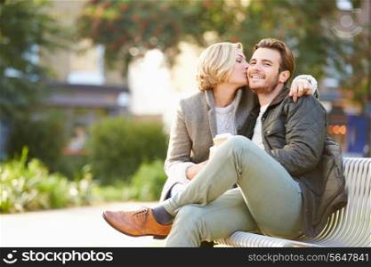Couple Relaxing On Park Bench With Takeaway Coffee