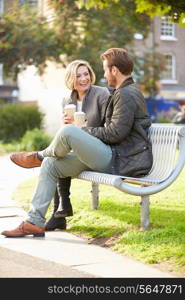 Couple Relaxing On Park Bench With Takeaway Coffee