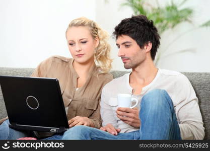 Couple relaxing on sofa with coffee and laptop