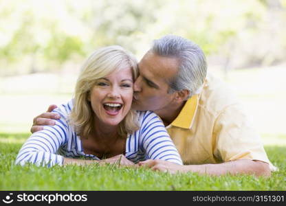 Couple relaxing outdoors in park kissing and smiling