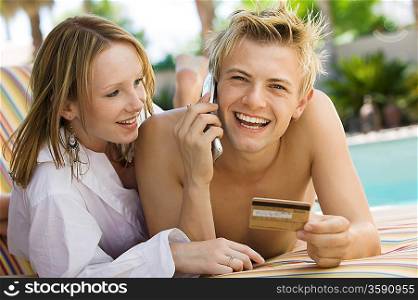 Couple Relaxing Poolside Using Credit Card and Cell Phone