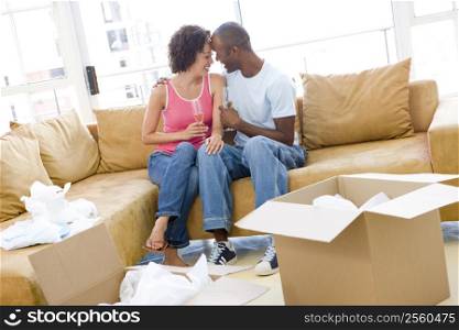 Couple relaxing with champagne by boxes in new home smiling