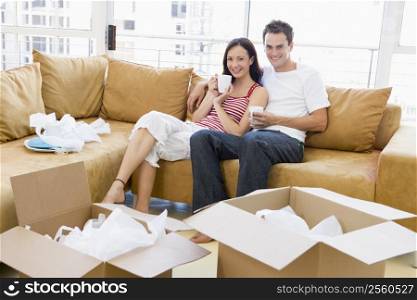 Couple relaxing with coffee by boxes in new home smiling