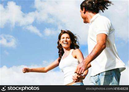 Couple running and smiling while having fun under sky