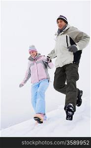 Couple running down snow-covered hill low angle view