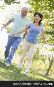 Couple running outdoors in park by lake smiling