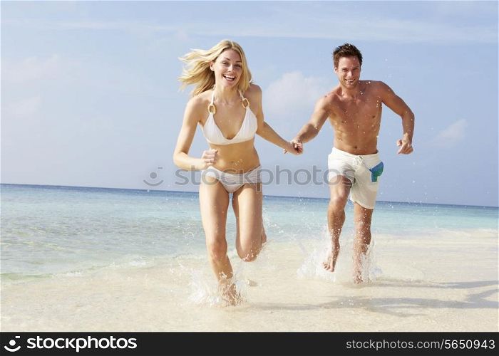Couple Running Through Waves On Beach Holiday