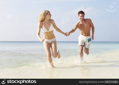 Couple Running Through Waves On Beach Holiday