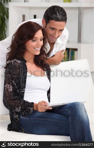 Couple sat at home looking at laptop screen