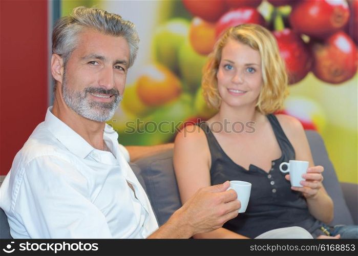 Couple sat on couch holding cup of drink