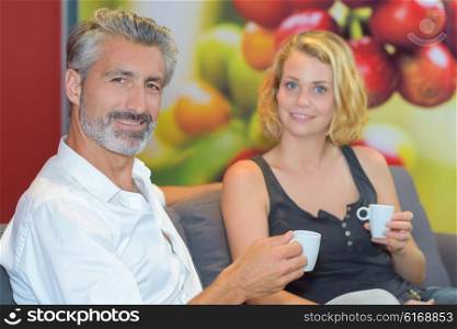 Couple sat on couch holding cup of drink