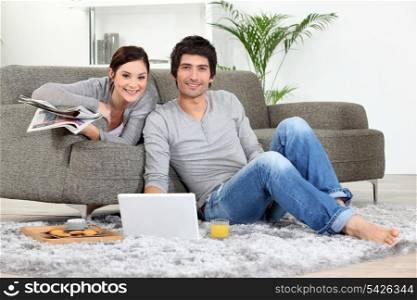 Couple sat on couch with laptop and newspaper
