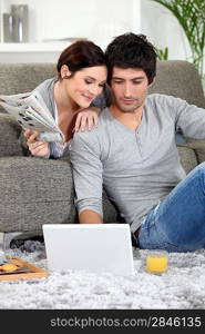 Couple sat on couch with newspaper and laptop