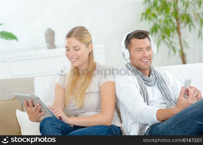 Couple sat on sofa, each using technology
