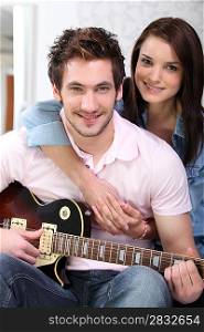 Couple sat on the couch with electric guitar
