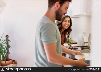 Couple sharing household chores. Happy woman watching man washing dishes.