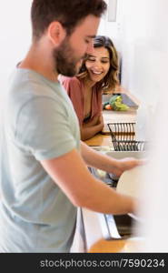 Couple sharing household chores. Happy woman watching man washing dishes.