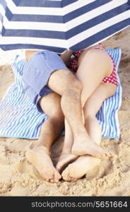 Couple Sheltering From Sun Under Beach Umbrella