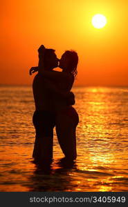 Couple silhouette ebraces and kisses in sea on sunset