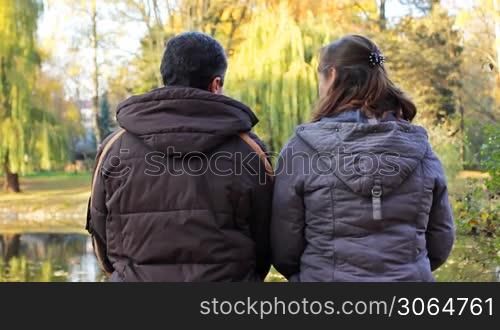 couple sits in beautiful autumn park near lake, then he hugs her, closeup