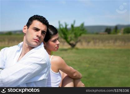couple sitting back to back in a field