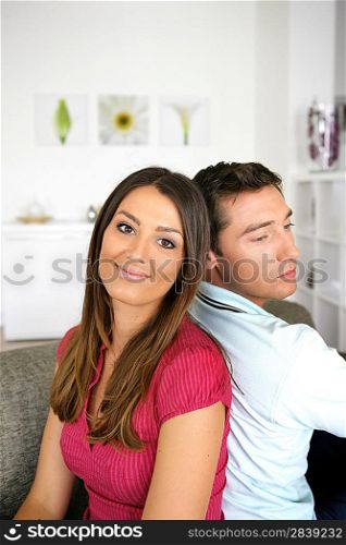 Couple sitting back to back on a sofa