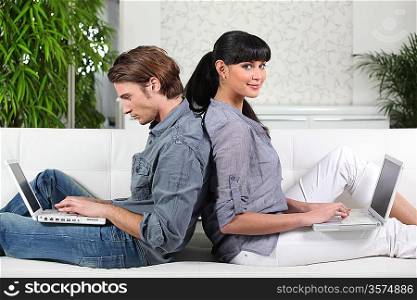 Couple sitting back to back on a sofa