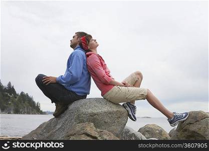 Couple sitting back to back on rocks by ocean